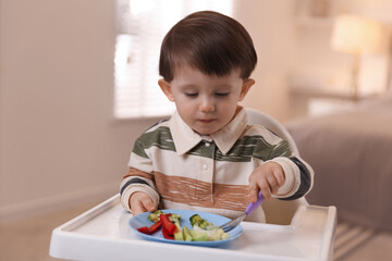 Cute little baby eating healthy food in high chair at home