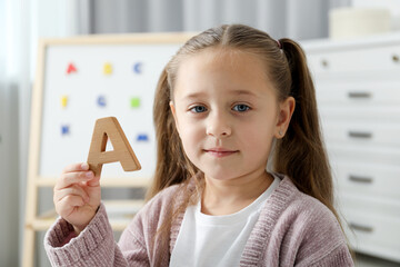 Learning alphabet. Little girl with wooden letter A indoors