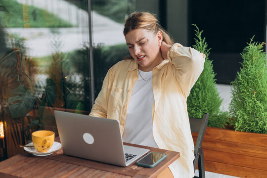 Entrepreneur freelancer overstudying and feeling bad sitting at the table. 30s woman with neck pain, stressed, sitting in front of laptop outdoors. High quality photo