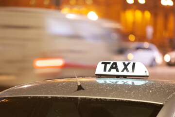 Shining Taxi inscription close up against passing cars on night street of big citi