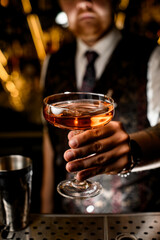 Male bartender showing a brown cocktail in a glass on a tall stem