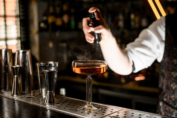 Focus on stemmed wine glass filled with brown cocktail being sprayed