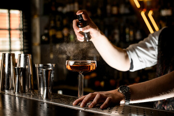 Close-up of male bartender's hand spraying glass of brown drink