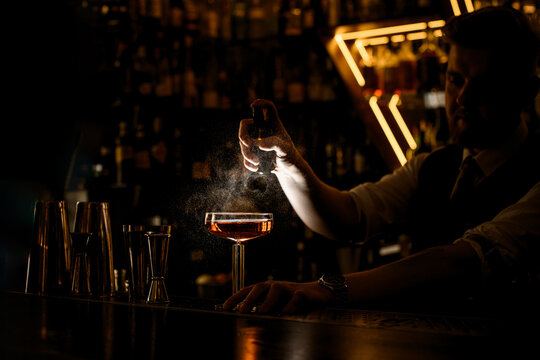 Bartender sprays glass with brown cocktail, on bar counter - Powered by Adobe