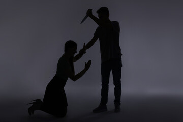 Domestic violence. Silhouette of man with knife threatening his wife on grey background