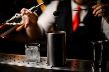 Bartender pours a brown drink from a long bar spoon into a metal glass