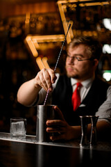 Bartender stirs a cocktail in a tall metal glass with a long bar spoon