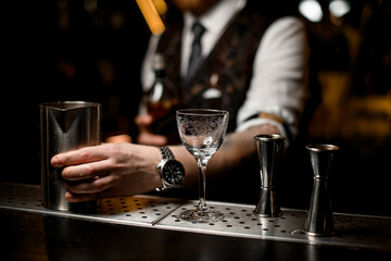 Metal mixing glass, cocktail jiggers and a wine glass stand on a metal bar stand
