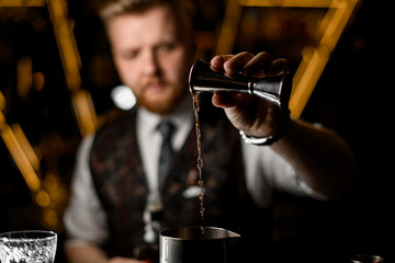 Bartender's hand pours a thin stream of liquid from a jigger into a metal glass