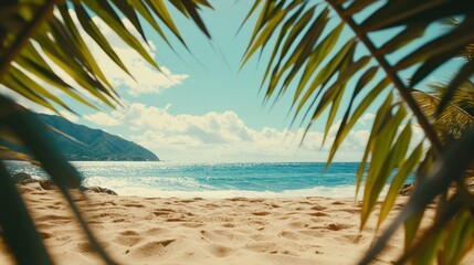 Sunny beach with soft sand and turquoise water seen through the leaves of palm trees on a warm day