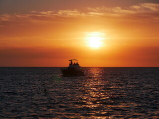 Fototapeta premium A romantic bright red sunset over the sea, a small yacht sails on the horizon, illuminated by the warm setting sun, scenic.