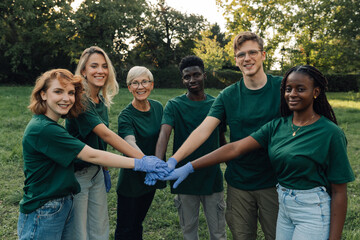 Group of volunteers putting hands together wearing gloves in park