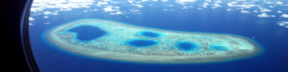 Obraz premium Atoll viewed from airplane window, surrounded by deep blue ocean. Concept of tropical island paradise. For travel website header.