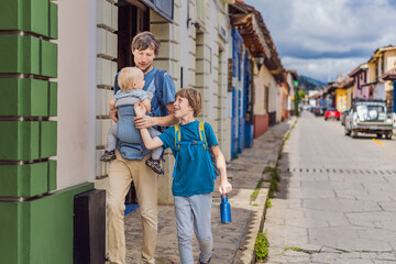 Fototapeta premium Father and and his two sons, a teenager and a baby tourists walks through the colonial streets San Cristobal de las Casas, Mexico. Cultural exploration, architecture, and travel experience concept