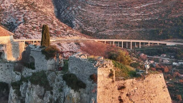 An aerial view of the A1 highway as seen from the historic ruins of Klis Fortress in Croatia. This stunning shot combines the modern highway with the scenic Dalmatian landscape and historic ruins.