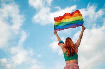Woman holding rainbow flag celebrating lgbtq plus pride with cloudy sky