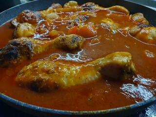 Georgian chicken stew with tomatoes and herbs (chakhokhbili) in cast iron skillet on dark stone background. Baked chicken with tomato vegetable gravy.