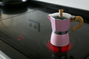 Pink Italian aluminum coffee pot and wooden handle placed on a ceramic hob