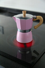 Pink Italian aluminum coffee pot and wooden handle placed on a ceramic hob