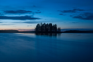 Obraz premium Late evening scenery of a calm lake with a wooden island in the forests of Finland