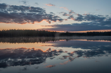 Clouds and forests reflected on the surface of a calm lake in Finland
