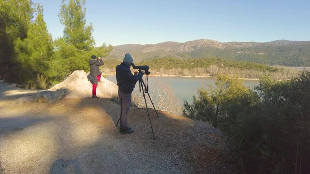 Birdwatchers observing birds in the lake with a telescope in winter. 