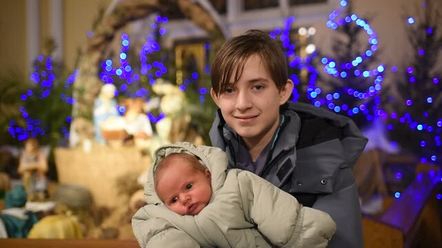 boy with baby brother in catholic church in front of nativity scene during christmas time	