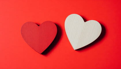 Two wooden hearts, one painted red and the other natural, placed on a bright red background.
