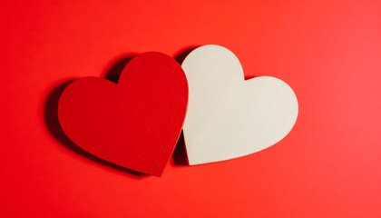 Two wooden hearts, one painted red and the other natural, placed on a bright red background.