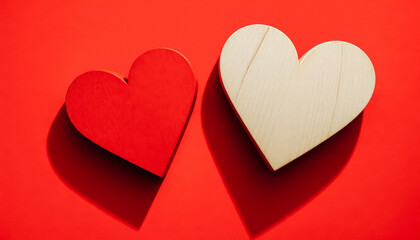 Fototapeta premium Two wooden hearts, one painted red and the other natural, placed on a bright red background.