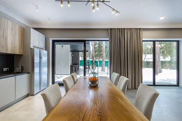 The interior of a country house with a kitchen set and a dining table made of a single piece of wood. Panoramic windows with a view of the winter landscape.