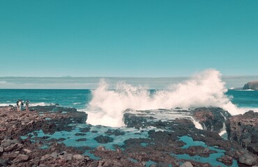 waves crashing on rocks, people making pictures.