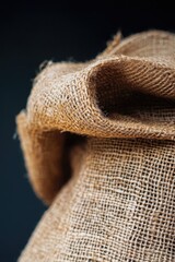A close up of a piece of burlap fabric with a dark background. The fabric has a rough texture and he is worn and frayed