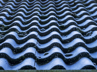 A roof is made of tiles and and covered with frost and has a blue color cast from clear sky. Winter cold season concept.