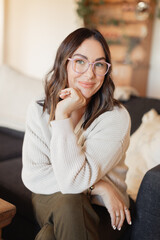 Therapist wearing glasses and a cozy sweater, smiling warmly indoors.