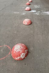 Red restrictive hemispheres on the asphalt road in the parking area of the car and the pedestrian area of walking people at the street. Area for foot people