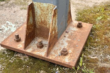 Metal pillar fastened to basement with anchor bolts and nuts. The rusty surface of the post and the fastenings are in places. The support of the iron black pillar on a green lawn in the park
