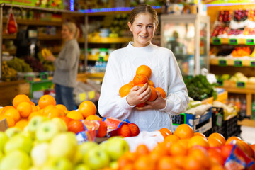 Interested smiling girl making purchases in supermarket, looking for fresh sweet oranges ..