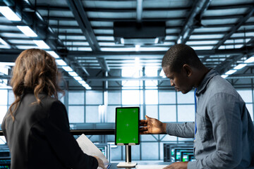 Technicians in data center using green screen mockup tablet, reviewing hardware diagnostics,...