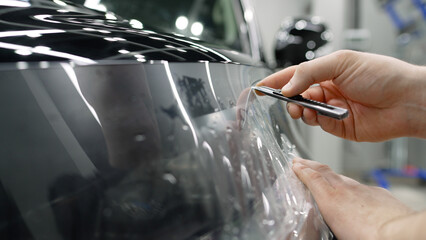 Professional mechanic carefully applying vinyl wrap to vehicle body in auto workshop, transforming...