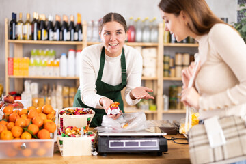 European saleswoman sells chocolates by weight and packs them in a bag. Seller weighs low-calorie candies on the scales. Buying natural delicious sweets.