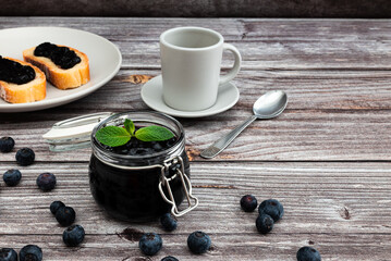 Delicious breakfast with homemade blueberries and mint jam. Glass jar with blueberries marmalade and mint leaves.