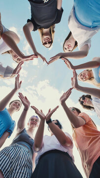 School friends joining hands to form heart shape against cloudy sky, representing unity, friendship, and teamwork