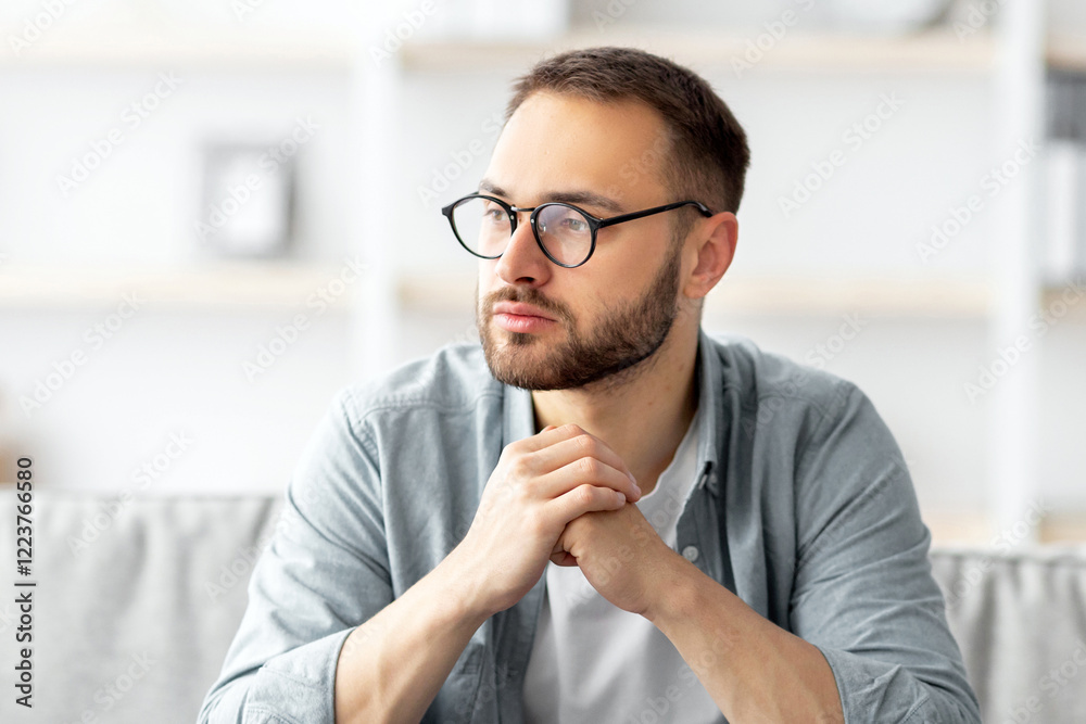 Aufkleber serious young caucasian guy sitting on couch in front of laptop computer at home. thoughtful millenn