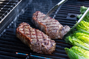 Juicy steaks and romaine lettuce on a grill close-up