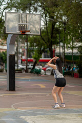 Fototapeta premium Young latin woman shooting at the basket on a public basketball court