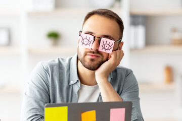 Workaholism, exhaustion at workplace concept. Tired young man having stickers with open eyes...