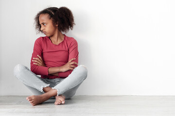 Sad black lady mother and upset female kid teenager daughter, having fight, quarrel, misunderstanding, sitting together on floor over white empty wall, copy space between mom and child