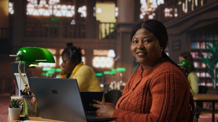 Portrait of african american librarian working in a peaceful public library, offering guidance and academic expertise to students. Woman manages educational personalized materials. Camera A.
