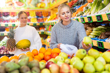 Mom and her teen daughter pick pineapple and melon at the grocery supermarket